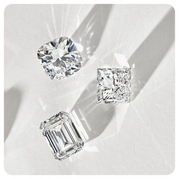 Three loose diamonds in cushion, princess, and emerald cuts on a light gray background with sharp shadows.
