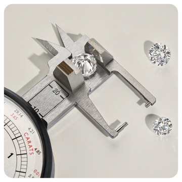A diamond carat caliper measuring a round brilliant-cut diamond, with two loose diamonds displayed on a light beige background.